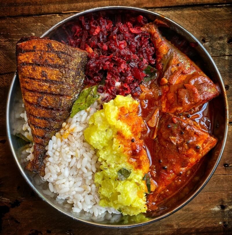 A vibrant South Indian meal featuring spicy fish curry, rice, and vegetables in a stainless steel bowl.