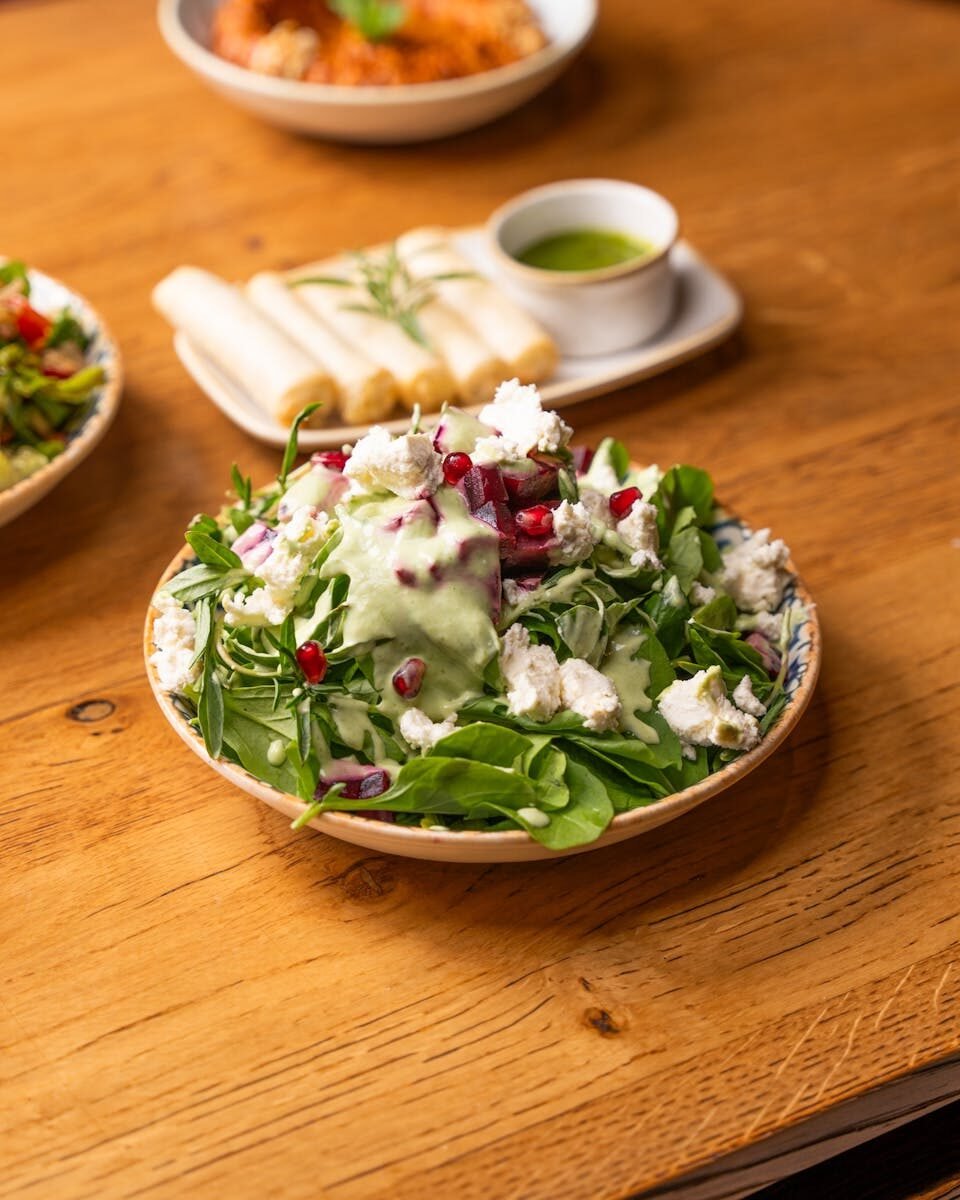 Delicious arugula salad with feta and pomegranate served on a rustic wooden table.