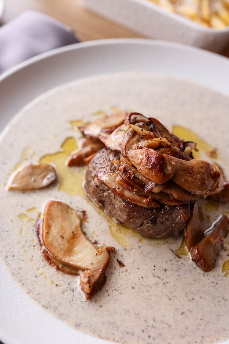 A delicious gourmet steak topped with wild mushrooms in a creamy sauce, elegantly plated.