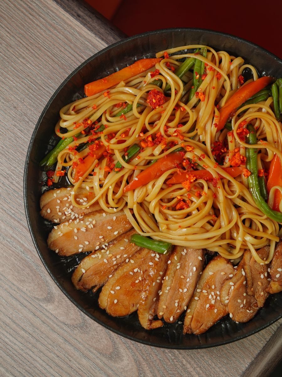 A flat lay of chicken teriyaki noodles with vegetables, sesame seeds, and vibrant colors.