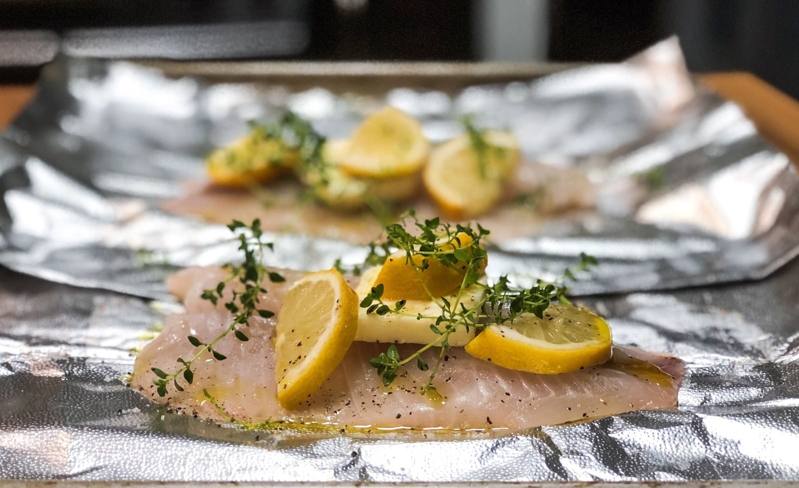 Close-up of salmon fillet topped with lemon slices and thyme on foil, ideal for culinary themes.