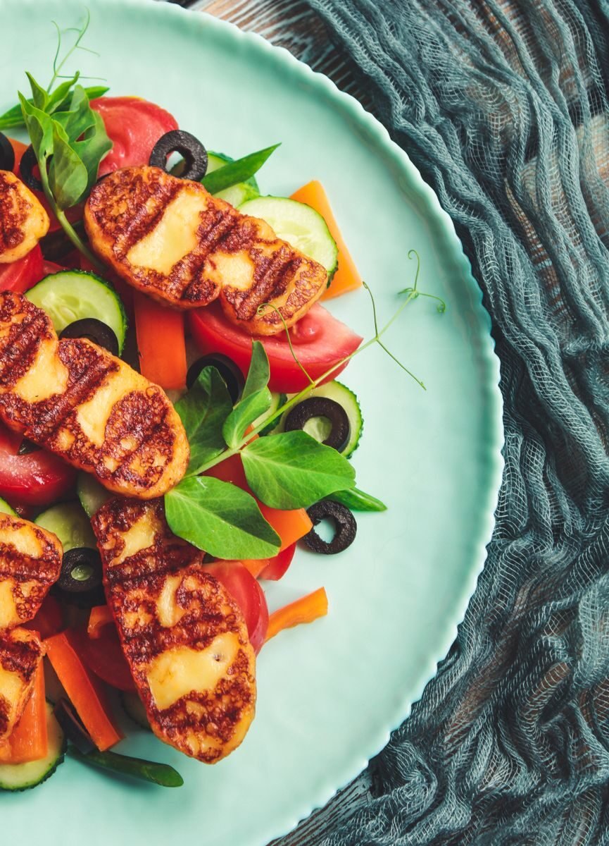 A delicious haloumi salad with fresh vegetables, grilled cheese, and herbs presented in an artistic flat lay.