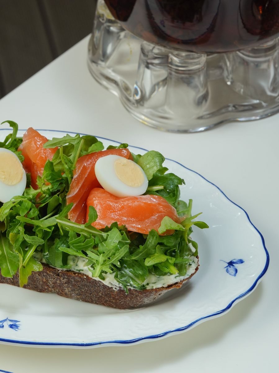 A fresh salmon, egg, and arugula open sandwich on a rustic plate.