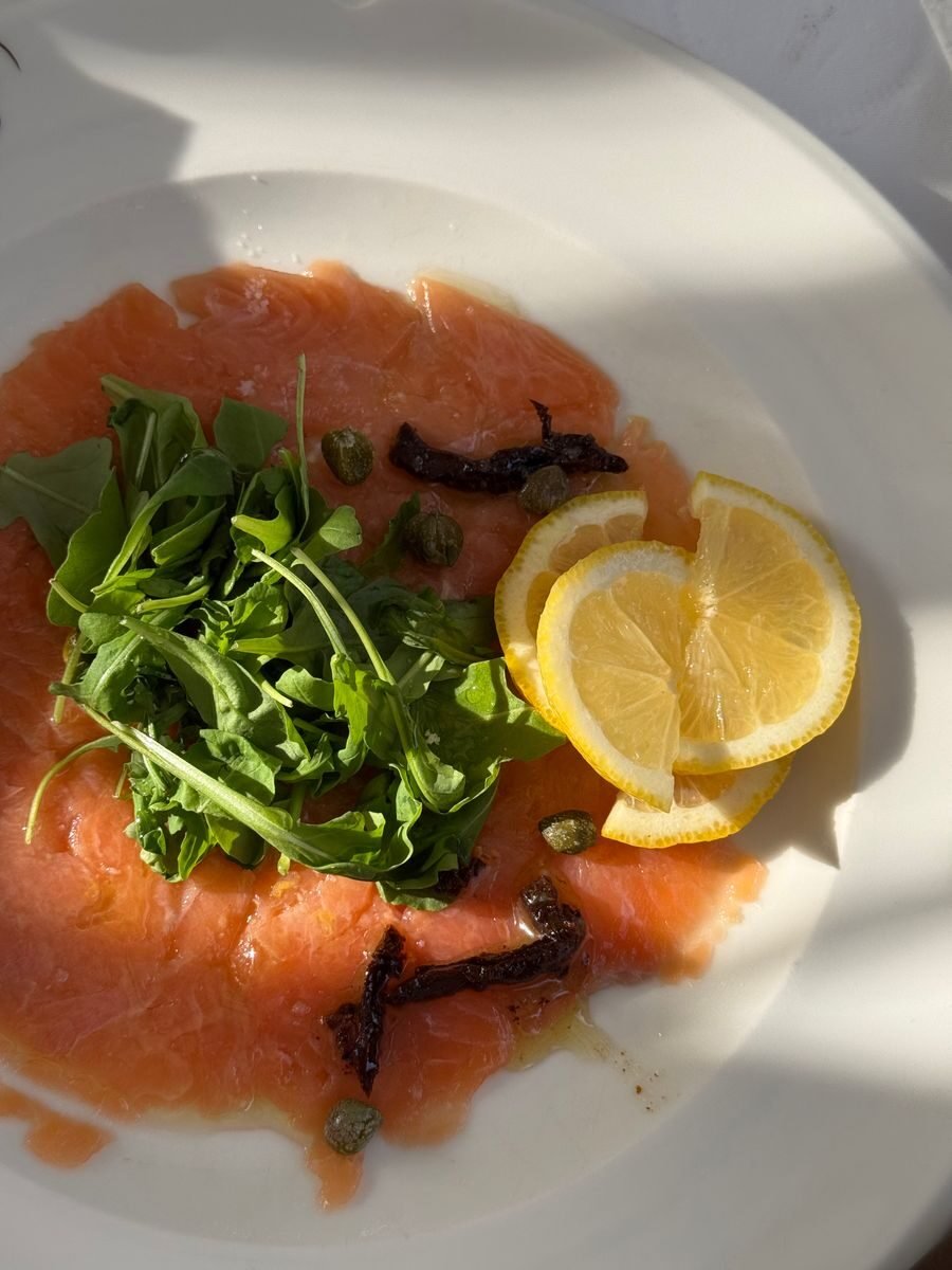 Delicious salmon carpaccio garnished with arugula, capers, and lemon slices.